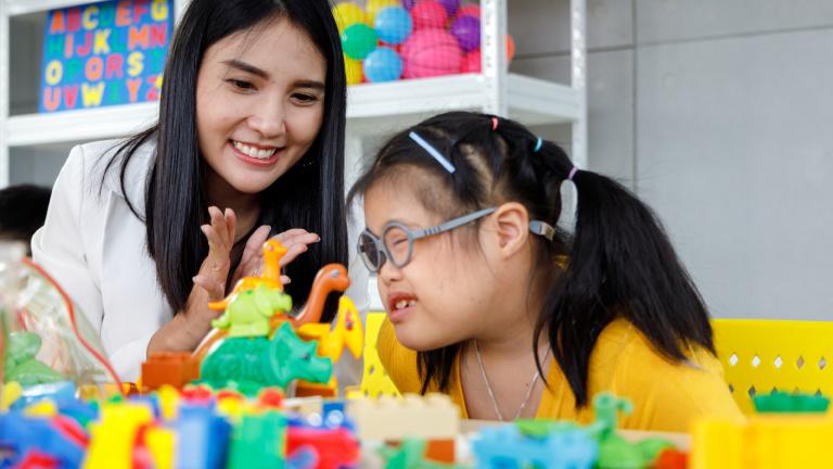 Photo of a woman interacting with a girl who is wearing therapeutic glasses and surrounded by educational toys.