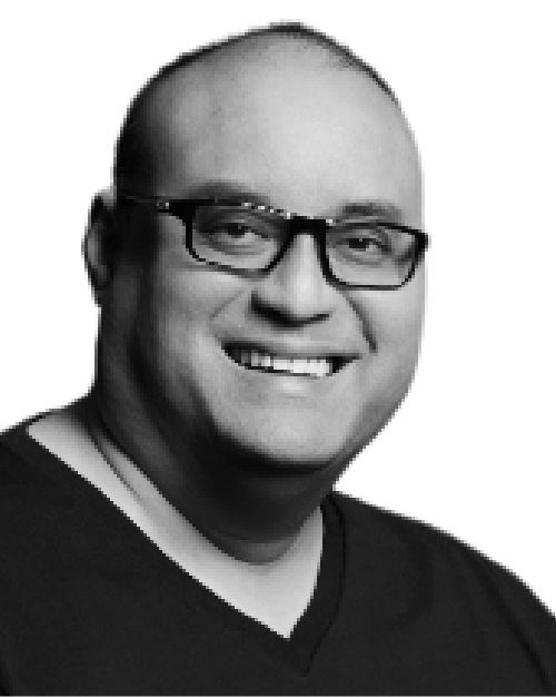 Black and white photo of Richard Kuppusamy, he is smiling, wears glasses and is wearing a black t-shirt